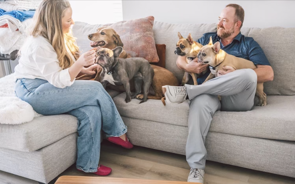 Two people sitting on a couch with three dogs.